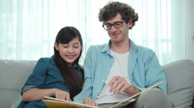 Mutlu kız babaya yaslanır hikaye anlatırken. Genç Asyalı liseli kız birlikte masal kitabı okurken ve kanepede otururken babasını arıyor. Aile eğlence konsepti. Pedagoji.