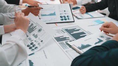 Bir grup profesyonel, masaya serilmiş çeşitli iş haritaları ve grafikleri analiz ederek kritik veri içgörülerini vurgulayarak toplantı sırasında işbirliği yapıyor. SACTR