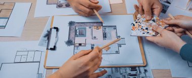 Çeşitli bireylerden oluşan bir grup modern bir çalışma alanında tasarım planları ve çizimler üzerinde işbirliği yapmaktadır. Çeşitli malzemeler ve aletler, takım çalışması ve yaratıcılığın gösterildiği bir masaya dizilmiştir. SACTR