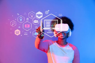Sanal gerçeklik kulaklığı takan, dijital pazarlama elemanlarıyla etkileşime geçen, müşteri ilişkilerinin ve içerik oluşturmanın geleceğini gösteren canlı bir görüntü. XDMCP