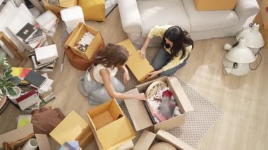 Mobilyaları kutudan indirirken mutlu oda arkadaşı kutusunu indirirken yukarıdan aşağıya doğru. Kız arkadaş ya da lezbiyen yeni bir eve ya da daireye taşınıyor ve etrafı kutularla çevrili oturma odasında oturuyor. Myrmidon.