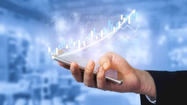 Bir el, finansal verileri ve büyüme grafiğini gösteren bir akıllı telefonu tutuyor. Modern ofis arka planı dijital analitik ve iş eğilimlerine odaklanmayı artırmaktadır. Etki