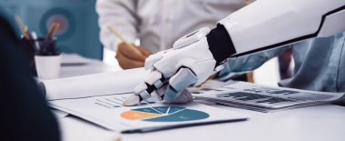 Robotik bir el, modern bir ofiste iş raporları ve grafikleriyle etkileşime geçerek, teknolojilerin takım çalışmasındaki rolünü ve üretkenliği artırmak için proje analizini vurgular.