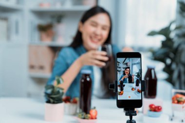 Seçici odaklı akıllı telefon ve gülümseyen genç, güzel Asyalı karışık çilek ve kiraz suyu detoksu değerlendirmesi sosyal medyada sağlıklı ürün tanıtımı sunuyor. Taktik.