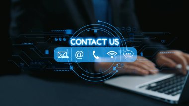 Bu stok görüntüsü modern bir kontak bizimle iletişim kuruyor bir dizüstü bilgisayarın üzerini örtüyor, karanlık bir kurumsal ortamda ellerini gösteriyor, iş iletişimi araçlarını vurguluyor. Dörtgen