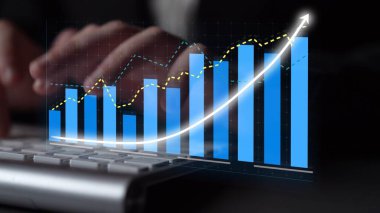 Bir klavye üzerinde ellerini gösteren profesyonel bir ayar, bar grafikleri ve çizgi grafikleriyle çeşitli veri eğilimlerini analiz eden, iş büyümesini ve performans anlayışını sembolize eden. Copula