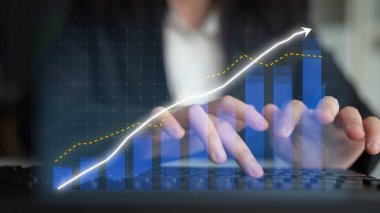 Veri analizi yapan bir iş kadını, bir dizüstü bilgisayarda grafikle örtüşen, profesyonel ofis ortamında büyümeyi ve modern teknolojiyi sembolize eden bir yazı yazıyor. Copula