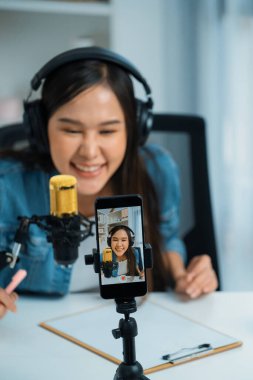 Asyalı sunucu canlı yayında canlı yayında canlı yayında sosyal medyada kulaklık takarak konuşuyor. Dinleyicileri modern stüdyoda koçluk yaparak selamlıyor. Taktik.