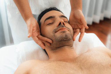 Beyaz adam stres önleyici kafa masajından ve lüks bir tatil beldesi veya otel spa salonundaki modern ışık ortamında yüz güzelliği eğlencelerini şımartmaktan hoşlanıyor. Sessiz.