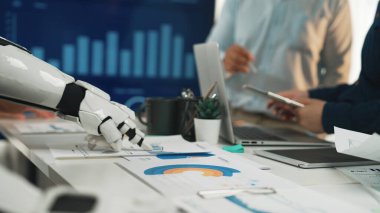 Robot bir kolun iş belgeleriyle etkileşime geçtiği, stratejik gelişim için veri analizinde işbirliği ve teknolojiyi vurguladığı modern bir ofis sahnesi. Noogenesis