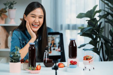 Gülümseyen, güzel Asyalı genç, lezzetli karışık çilek ve kiraz suyu detoksu içeceklerini inceleyen, sosyal medyada özel promosyon satışı için sağlıklı ürünler sergileyen. Taktik.