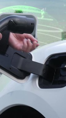 İlerleyen yeşil şehir ESG sembolü, elektrikli araçla birlikte. İş adamı EV arabalarını şarj etmek için şarj aletini şarj ediyor. Şehirdeki şarj istasyonunda ekolojik ve yeşil semboller var..