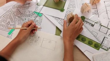 Mimar ve mühendis, mimari belge, ölçüm aracı ve ahşap bloğu ofis çevresinde dağıtan planlar kullanarak inşaat inşaatı hakkında düşünür veya tartışır. Tanımlama.