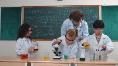 Kafkasyalı zeki öğretmen, meraklı öğrencilerin laboratuardaki deney kabına renkli sıvı dökmesini destekler. Yaratıcı çocuklar deney yapmaya ve biyokimyasal örnekleri incelemeye konsantre olurlar. Pedagoji.