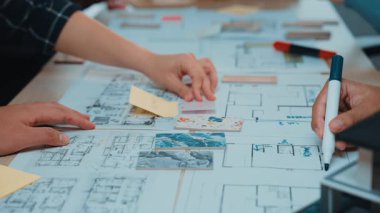 Mimari planlar üzerinde tasarım planlaması yapan, yaratıcı bir çalışma alanında beyin fırtınası ve takım çalışması yapan ellerin yer aldığı canlı bir işbirliği sahnesi. SACTR