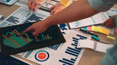 Bir tablet ve yazılı raporlar, takım çalışması ve stratejisini gösteren çeşitli grafik ve grafikleri analiz eden çeşitli bir iş ekibi, modern bir ofiste işbirliği yapıyor. SACTR