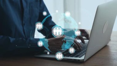 Küresel bağlantıyı temsil eden ve modern iş çözümleri için ağ oluşturan dijital simgelerle çevrili ahşap bir masada dizüstü bilgisayar kullanan bir birey. Dörtgen