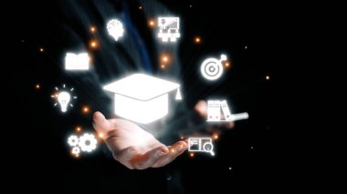 Eğitim ve yenilik sembolleriyle çevrili mezuniyet şapkası amblemini tutan bir elin dinamik görüntüsü bilginin ve başarının önemini gösteriyor. Dörtgen