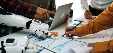 Çeşitli bir ekip, verileri analiz etmek ve çeşitli projelerde ilerleme kaydetmek için insanlarla birlikte robotik bir kol kullanarak modern bir çalışma alanında iş birliği yapmaktadır.