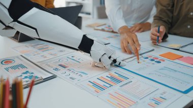 Grafikler ve grafikler içeren çeşitli veri analiz belgeleri üzerinde çalışan bir insan ve robotu gösteren modern bir ofis sahnesinin yakından bir görüntüsü.