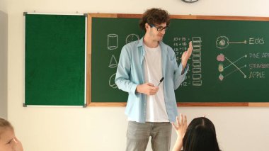 Matematik formülü veya teorisi ile karatahtanın önünde dururken sınıfın etrafına bakan profesyonel akıl hocası. Çeşitli ilköğretim öğrencileri matematik dersinde öğreniyor, çalışıyor ve oturuyor. Pedagoji.