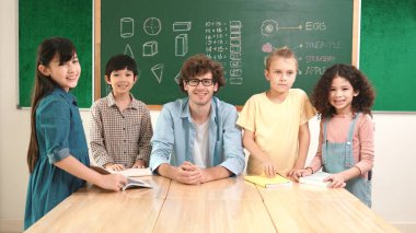 Profesyonel Kafkas öğretmeni ve çeşitli öğrenciler kameraya bakarken mutlu okul çocuğu gülümsüyor. Sınıfın önünde dururken gülümseyen bir grup çok kültürlü çocuk. Eğitim. Pedagoji.