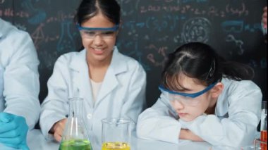 Zeki öğretmen, çeşitli deneyler yapan çocuklara destek olur ve onlarla ilgilenir. Karışık ırktan lise öğrencisi masadaki biyokimyasal sıvıyı mikroskop ile inceliyor. Öğretim