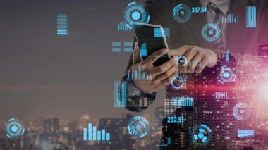 Profesyonel bir işadamı dijital grafikler ve veri analizleriyle çevriliyken akıllı bir telefonla iletişim kurar. Modern şehir silueti geceleri canlı bir zemin oluşturuyor. Xenic