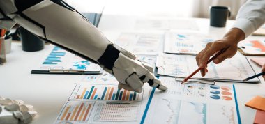 Modern bir ofiste veri analizi üzerinde çalışan bir insan eli ve robot kolu gösteren büyüleyici bir görüntü, takım çalışmasını ve teknoloji entegrasyonunu vurguluyor. Noogenesis