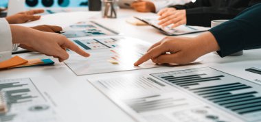 Çeşitli profesyonellerin grafik ve grafiklerin analiziyle ilgilendiği, modern bir ofis ortamında takım çalışması ve iletişimi ön plana çıkaran işbirlikçi bir iş toplantısı sahnesi. SACTR