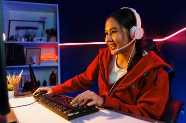 İnternet üzerinden kulaklık takıp gülümseyen Asyalı güzel kız flamasının sunucu kanalı izleyicilerle internet üzerinden konuşma yapıyor. Esport yetenekli takım oyuncuları neon mavi odada. Taktik.