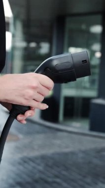 İlerici iş kadını şehir merkezinde dolaşmadan önce şarj cihazından elektrikli arabasına şarj prizi takıyor. Çevre dostu şarj edilebilir araba, sürdürülebilir ve temiz enerjiyle çalışıyor..