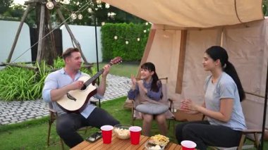 Baba gitar çalarken anne ve kız birlikte kampta oturuyorlar. Ebeveynler, genç nesil çapraz kuşak farklılıklarıyla zaman geçirmek için açık hava kamp aktivitelerini kullanıyorlar. Uyumsuzluk.