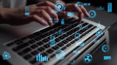 Modern bir çalışma alanında analitik ve dijital teknolojiyi temsil eden fütüristik veri görselleştirmeleriyle geliştirilmiş bir dizüstü bilgisayarın klavyesine yazı yazan ellerin yakın plan görüntüsü. Xenic