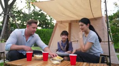 Aile hep birlikte bahçedeki kampta oturup yemek yiyor. Ebeveynler, genç nesil arasında iletişim kurmak ve zaman geçirmek için açık hava kamp faaliyetlerini kullanıyorlar. Uyumsuzluk.