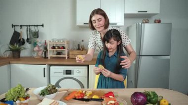 Akıllı beyaz anne ve Asyalı kız birlikte yemek pişirip kameraya poz veriyorlar ya da akşam yemeği için salata hazırlıyorlar. Mutlu anne ve kız taze yemekle sağlıklı yemek yapıyorlar. Sağlıklı gıda konsepti. Pedagoji.