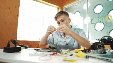 Akıllı mutlu çocuk araba modelini tamir etmek için elektronik alet kullanmayı öğreniyor ya da inceliyor. Lise öğrencisi STEM sınıfında otururken robotik makineleri tamir etmek için elektrikli teçhizat eğitimi alıyor. Öğretim