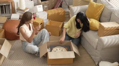 Lezbiyen aşıklar taşınma gününde karton kutudan nesneleri alıyorlar. Taşınırken paketleri açmak ve kutudan mobilya toplamak için birlikte çalışan bir çift oda arkadaşı. Yer değiştirme konsepti. Myrmidon.