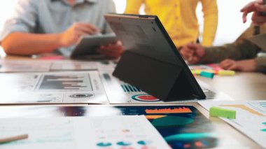 Çeşitli bir ekip, tabletler üzerindeki veri analizi ve modern ofis ortamında basılı belgeler üzerinde işbirliği yaparak verimli bir iş toplantısı düzenliyor. SACTR