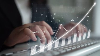 Bir iş adamı dijital grafik örtüsüyle temsil edilen finansal verileri incelerken klavyede yazı yazar. Bu resim modern ofis ortamındaki büyüme eğilimlerini gösteriyor. Copula