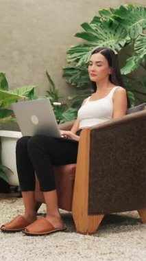 Modern genç kadın telefonda konuşuyor, uzaktan çalışıyor ya da tropik bitkilerle birlikte minimalist bir mimari beton stil yaz egzotik bitki yetiştirme bahçesinde yalnız başına dinleniyor. Blithe