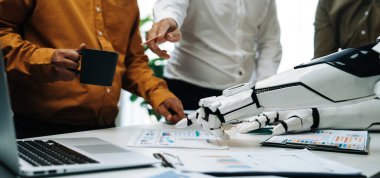 Dinamik bir ofis sahnesi kahve, çizelge ve belgelerle insanlar ve robotlar arasındaki etkileşimi gösteriyor, teknolojide işbirliğinin geleceğini gösteriyor. Noogenesis