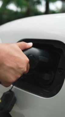 İlerici adam elektrikli aracına elektrik kablosu takıyor. Ev şarj istasyonundan EV arabası. Çevreyi korumak için temiz ve yenilenebilir enerji kullanan elektrikli bir araba. Çevre dostu otomobil.