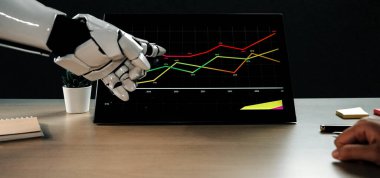 Robotik bir el, finansal verileri gösteren dokunmatik bir ekranla etkileşime girer. Dekoratif elementlerle tamamlanmış modern çalışma alanındaki büyüme eğilimlerini gösterir. Noogenesis