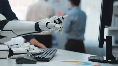 Gelecekçi bir robotik el, modern bir ofisteki bilgisayarla etkileşime geçmek için uzanır. İş yerindeki teknoloji ve insan işbirliğini sembolize eder. Noogenesis