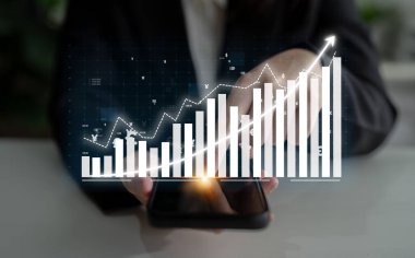 İş adamı, finansal grafikleri gösteren, büyüme ve başarı ölçümlerini gösteren akıllı telefonu inceliyor. Finans ya da teknoloji teması için mükemmel. Etki