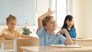 Sınıfta okuyan çeşitli çocuklarla çevrili beyaz bir çocuk öğretmenine soru sorup cevap verdiği için elini kaldırıyor. Mutlu öğrenci birlikte çalışıyor, oy veriyor, gönüllü oluyor, hocayı arıyor. Pedagoji.