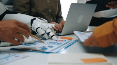 Bir insan ve bir robot modern ofis ortamında işbirliği yapar, verileri analiz eder ve stratejileri tartışır, teknoloji ve insan zekası arasındaki sinerjiyi gözler önüne serer.