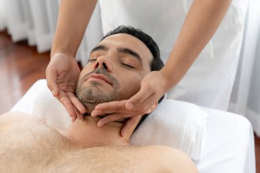 Beyaz adam stres önleyici kafa masajından ve lüks bir tatil beldesi veya otel spa salonundaki modern ışık ortamında yüz güzelliği eğlencelerini şımartmaktan hoşlanıyor. Sessiz.