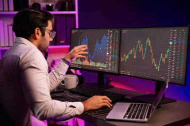 Akıllı tüccar işadamı, karanlık oda gecesinde neon ışıklı ofisteki arama pazarında yüksek kârla ekranda bilgisayar ve bilgisayar üzerinde dinamik borsa yatırımları üzerinde yoğunlaşıyor. Tahmin et..